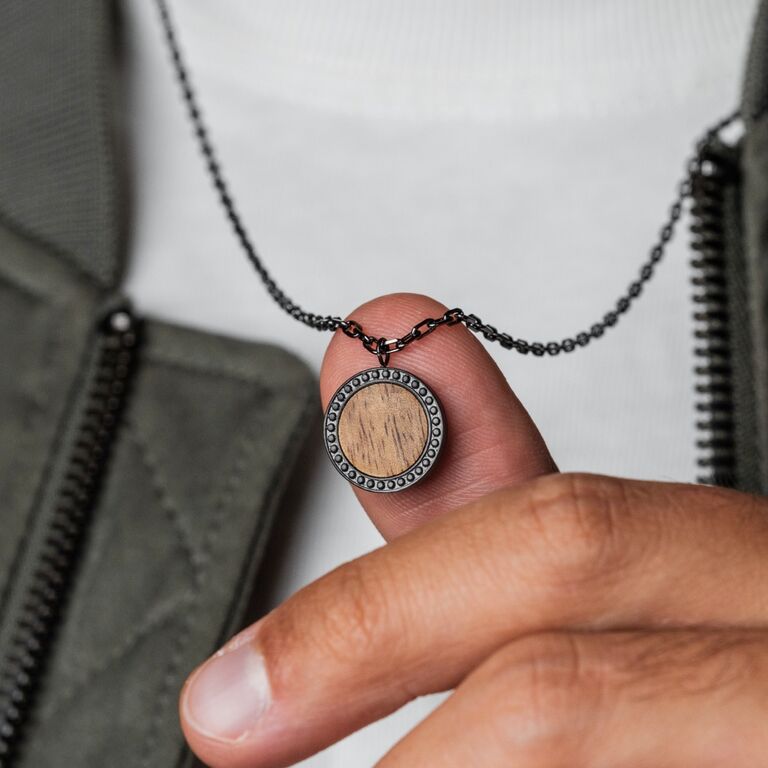 El collar "Collar Interplay" presenta un colgante circular con un centro de madera de koa y detalles grises, que ofrece un estilo moderno y terroso.